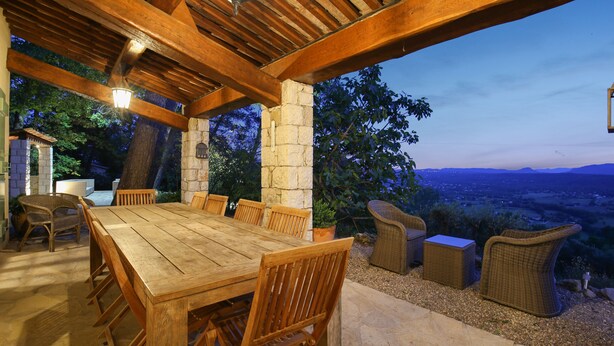 An outdoor wooden dining area with stone pillars, wicker furniture, and a view of the landscape. - Spectacular Views, Pool & 5-Bedroom Family-Friendly Holiday Home in Provence (Fayence)