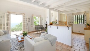 A spacious living area with a sofa, a coffee table, and a view of the outdoors. There is a kitchen area with a counter and cabinets. - Spectacular Views, Pool & 5-Bedroom Family-Friendly Holiday Home in Provence (Fayence)