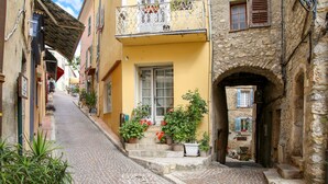 A narrow cobblestone street with buildings on either side, a yellow building with a balcony, and a stone archway. - Spectacular Views, Pool & 5-Bedroom Family-Friendly Holiday Home in Provence (Fayence)