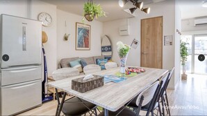 A modern kitchen with a refrigerator, a dining table with chairs, a sofa, and a hanging plant.