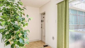 A room with a potted plant, a door, a window with a view of a building, and a tiled floor.