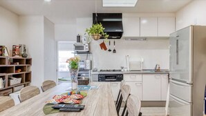 A modern kitchen with white cabinets, a stainless steel refrigerator, and a dining table set with chairs.