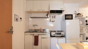 A compact kitchen with white cabinets, a gas stove, a microwave, and a refrigerator. - V.Close to Shinjuku Kabukicho/Korean Town/FrWIFI A (Shinjuku)