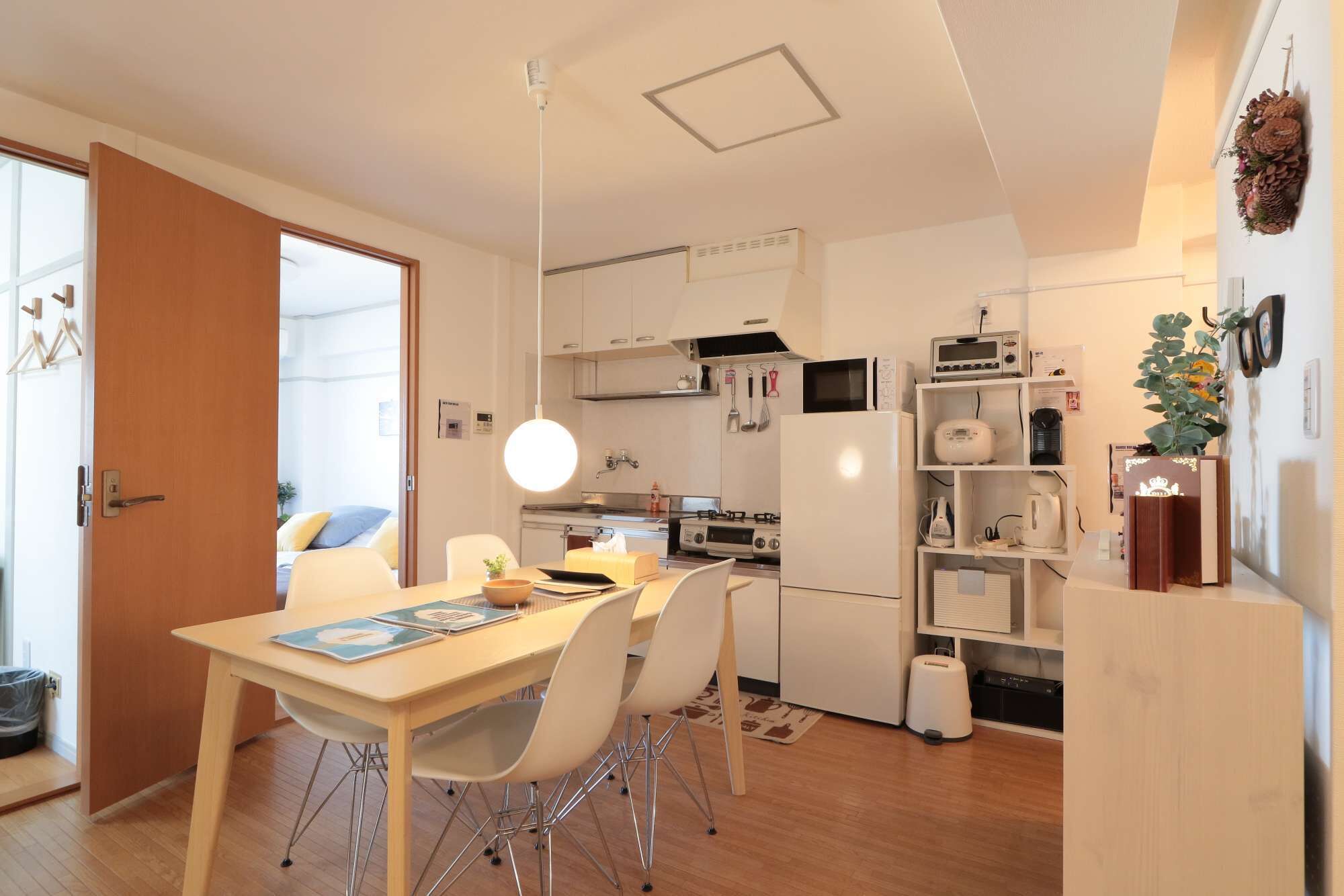 Eine moderne Küche mit weißen Schränken, einem Esstisch mit Stühlen, einer Hängeleuchte und einem Kühlschrank.