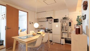 A modern kitchen with white cabinets, a dining table with chairs, a hanging light fixture, and a refrigerator. - V.Close to Shinjuku Kabukicho/Korean Town/FrWIFI A (Shinjuku)