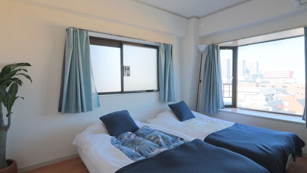 A hotel room with two beds, a potted plant, and large windows with curtains. - V.Close to Shinjuku Kabukicho/Korean Town/FrWIFI A (Shinjuku)