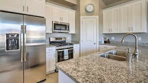 A kitchen with white cabinets, stainless steel appliances, a granite countertop, and a wall clock.