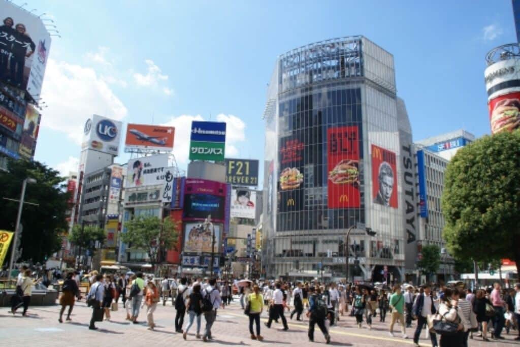 A busy urban square with modern buildings, large billboards, and pedestrians.