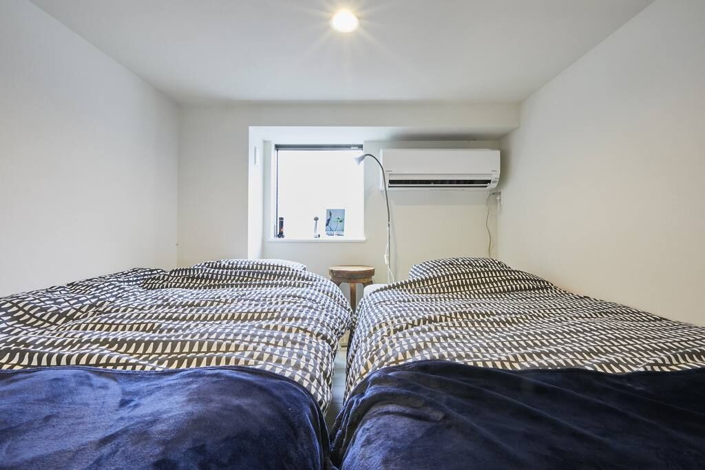 Una habitación pequeña y estrecha con dos camas, una ventana y un equipo de aire acondicionado.