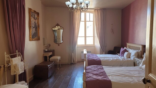 A bedroom with two beds, a vanity with a mirror, a dresser, a window with curtains, and a chandelier. - A relaxed,  comfortable and cosy home (Chef Boutonne)
