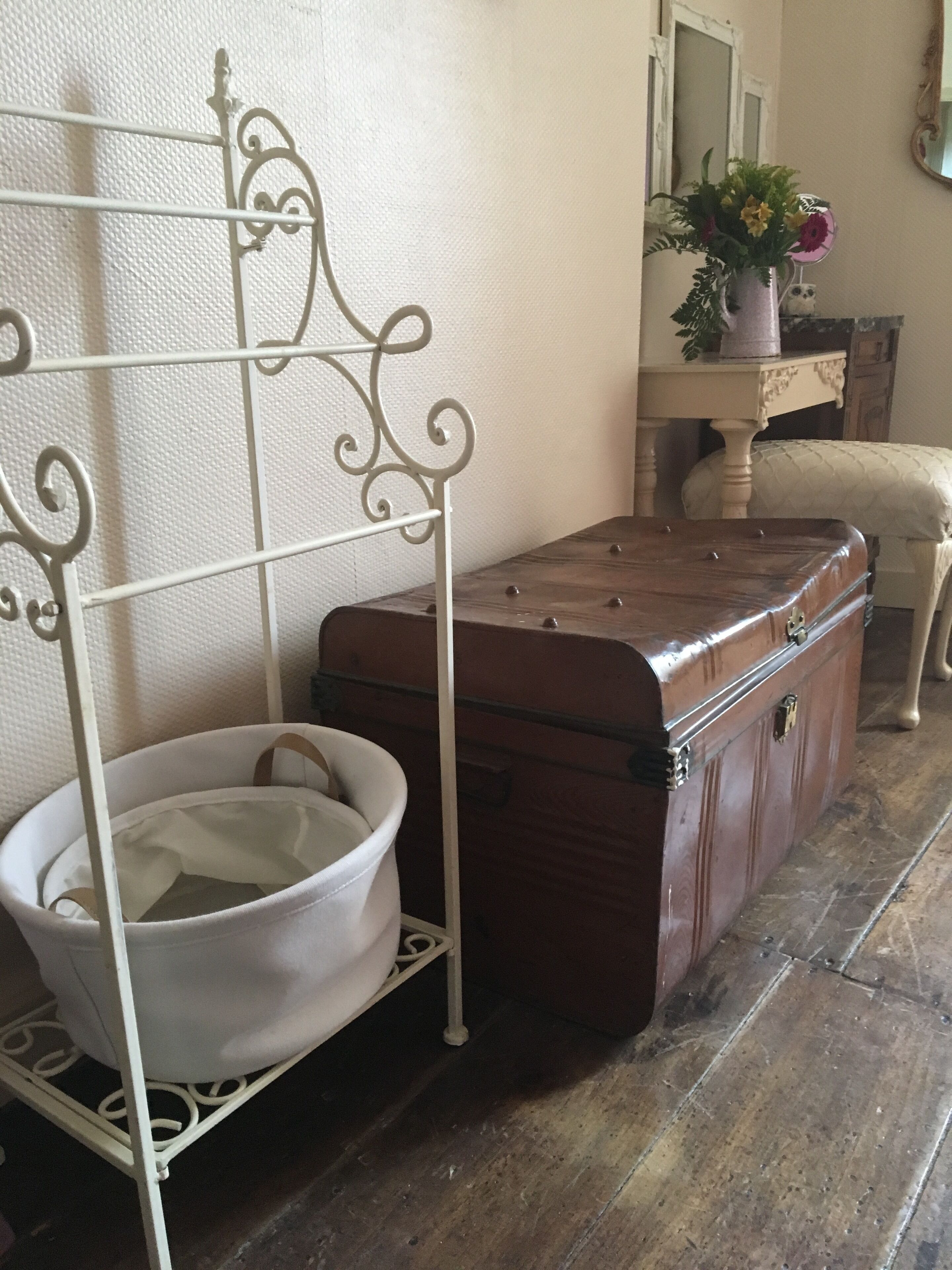 Una habitación de estilo vintage con un marco de cama de metal, un cofre de madera y un lavabo blanco.