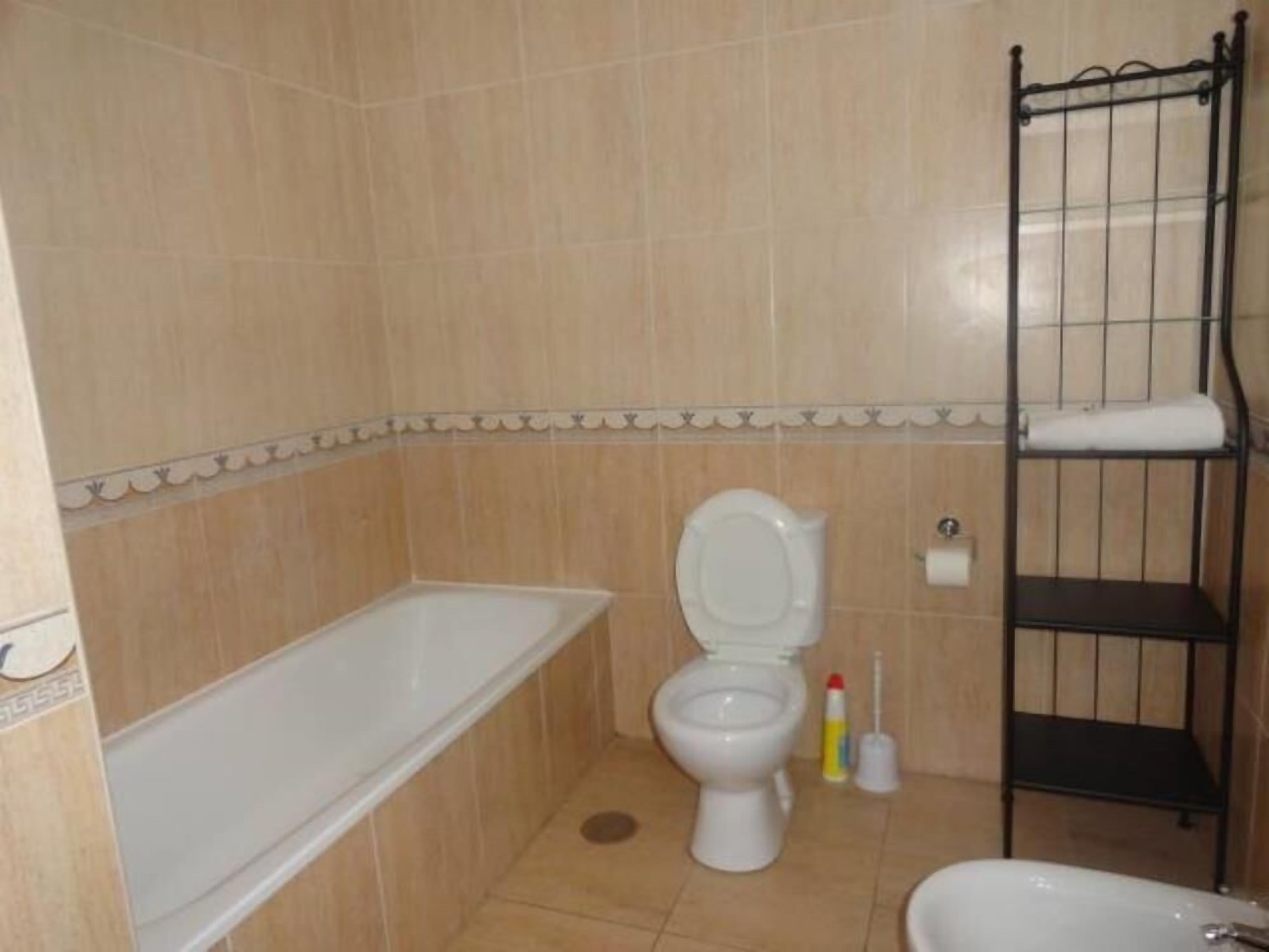 A bathroom with a toilet, a sink, a bathtub, and a metal shelf unit.