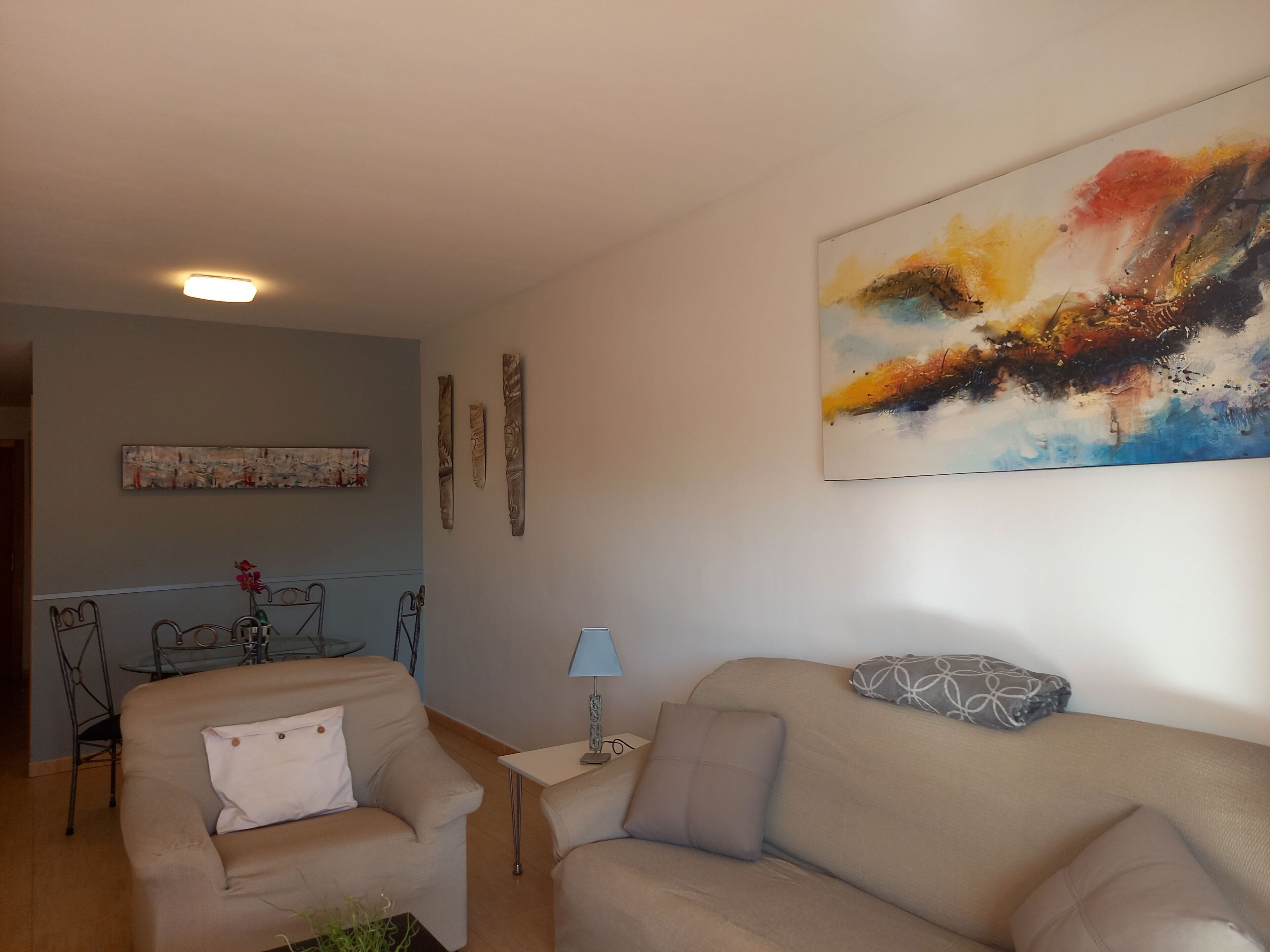 A living room with a beige sofa, a small table with a lamp, and a painting on the wall.