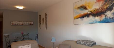 A living room with a beige sofa, a small table with a lamp, and a painting on the wall.