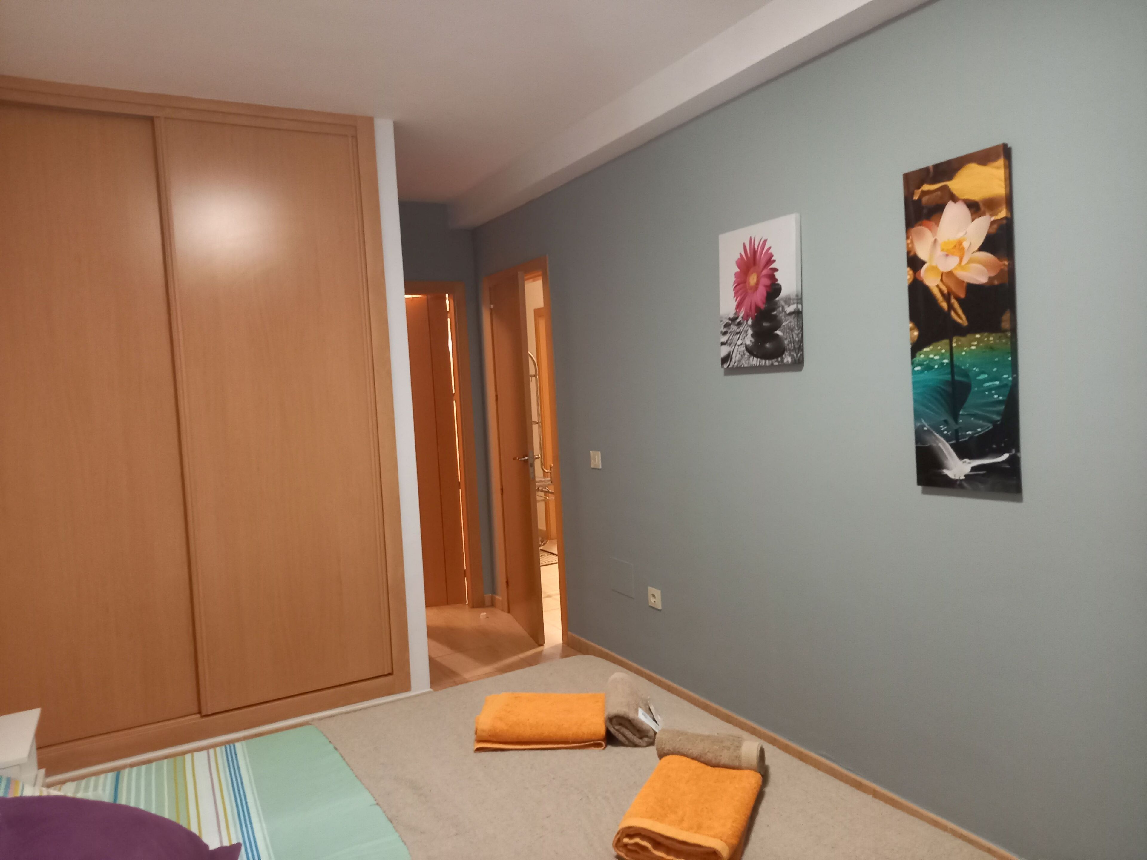 A bedroom with a large wardrobe, a bed with a striped bedspread, and two wall-mounted pictures.