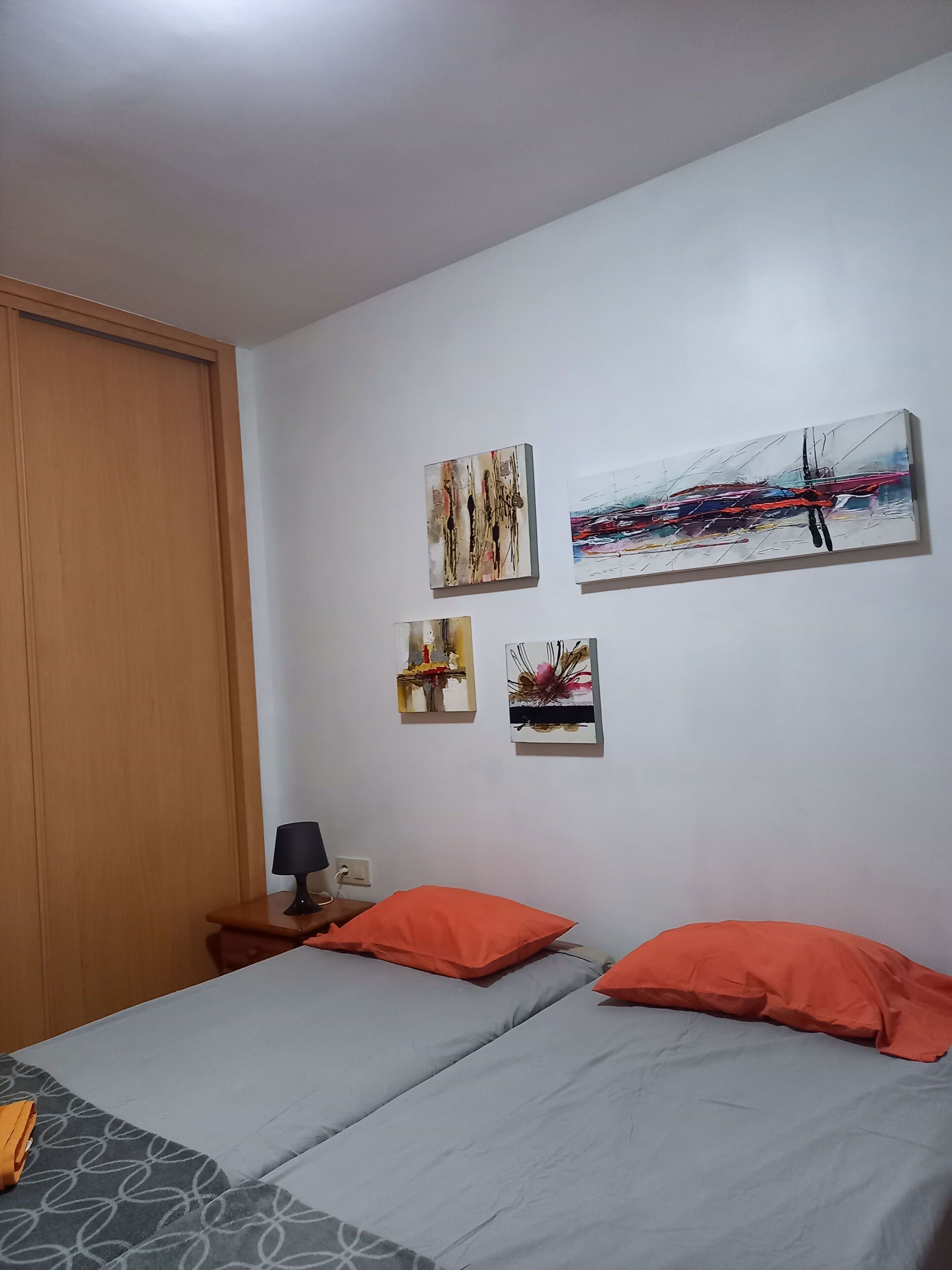 A bedroom with two beds, a wooden wardrobe, and three wall-mounted paintings.
