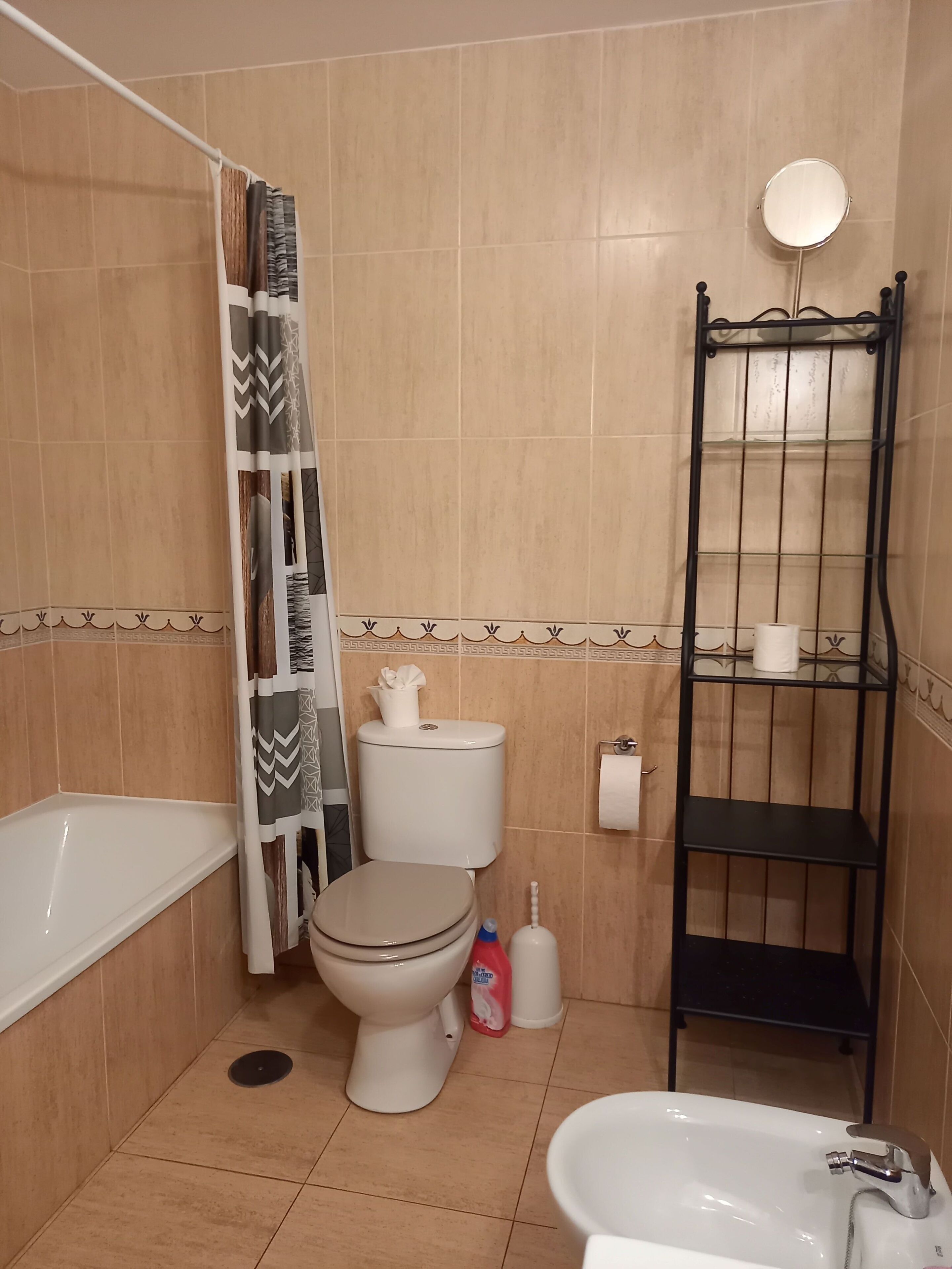 A bathroom with a toilet, bathtub, and sink. There is a shelf with toiletries and a mirror above the sink.