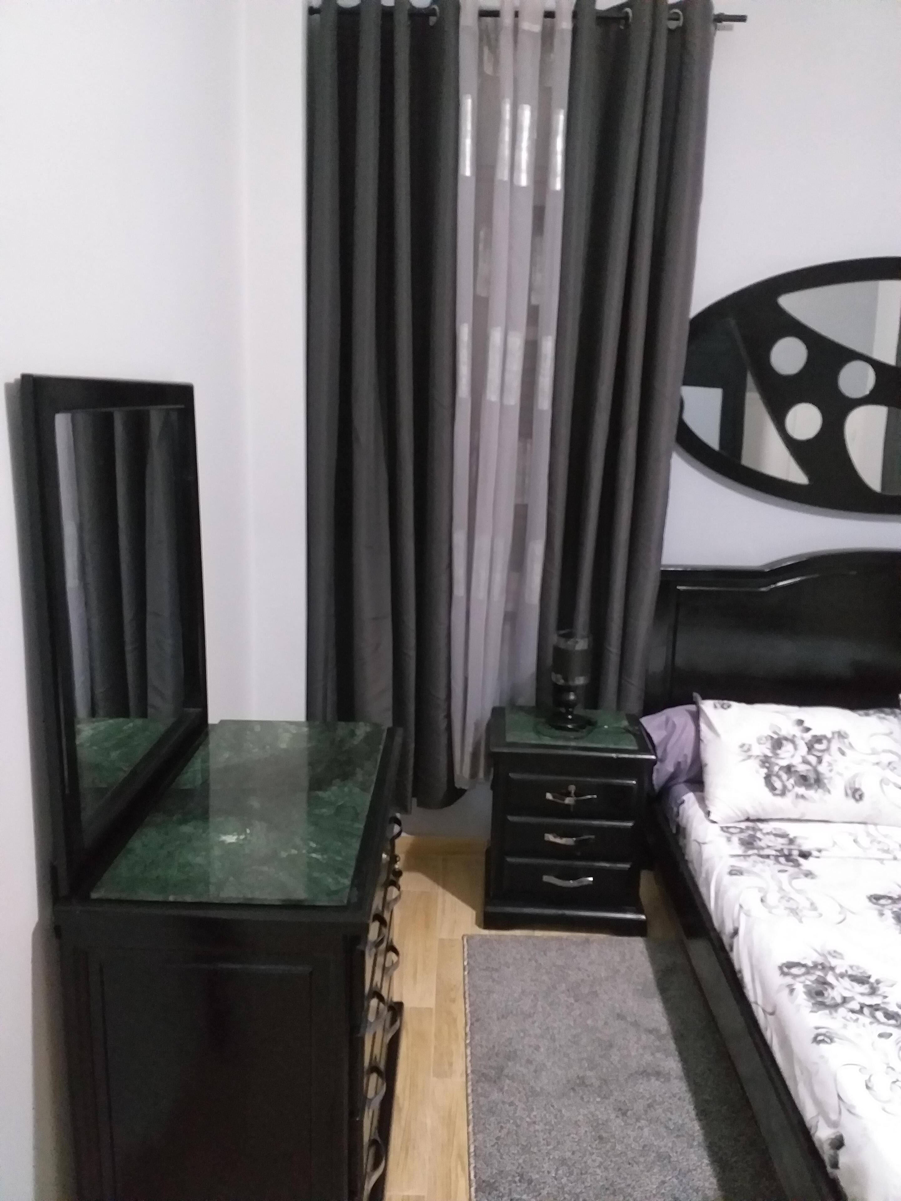 Une chambre à coucher comprenant un lit, une table de chevet, une commode, un miroir et un rideau.