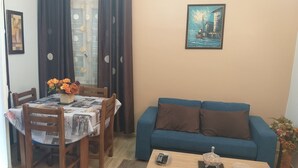 Olohuoneessa on sininen sohva, puinen sohvapöytä ja ruokailutila, jossa on katettu pöytä kahdelle.