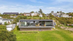Une maison moderne avec un toit plat, de grandes fenêtres et un balcon doté d’un espace salon extérieur.