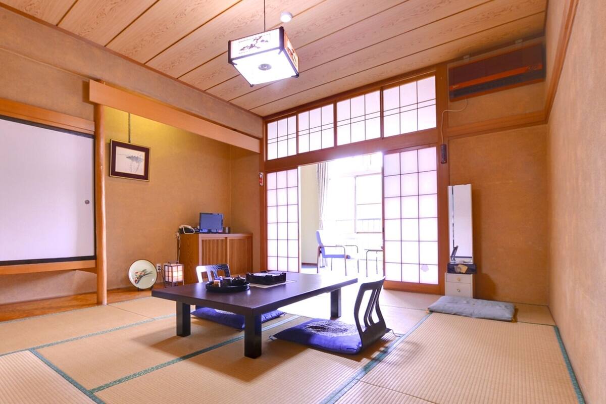Una tradizionale stanza giapponese con pavimento in tatami, un tavolino basso, una scrivania con un computer e porte scorrevoli.