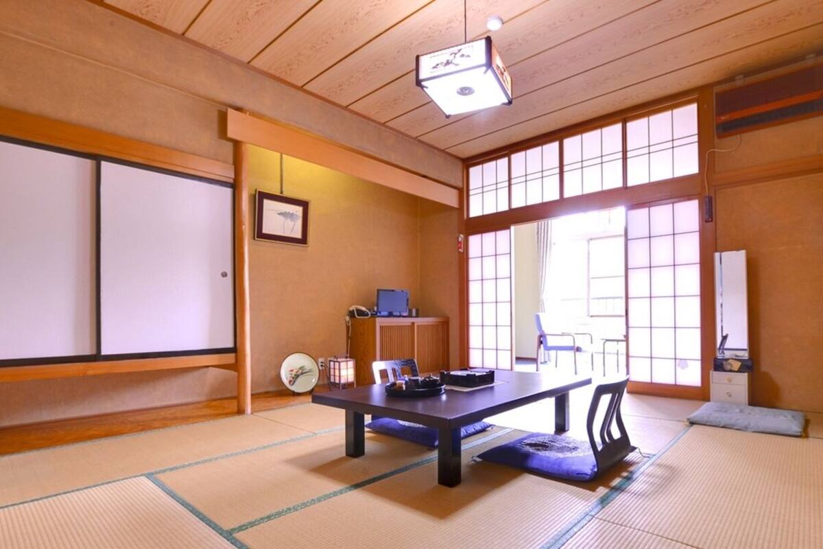 Una tradizionale stanza giapponese con pavimento in tatami, un tavolino con cuscini, una scrivania con un computer e porte scorrevoli.