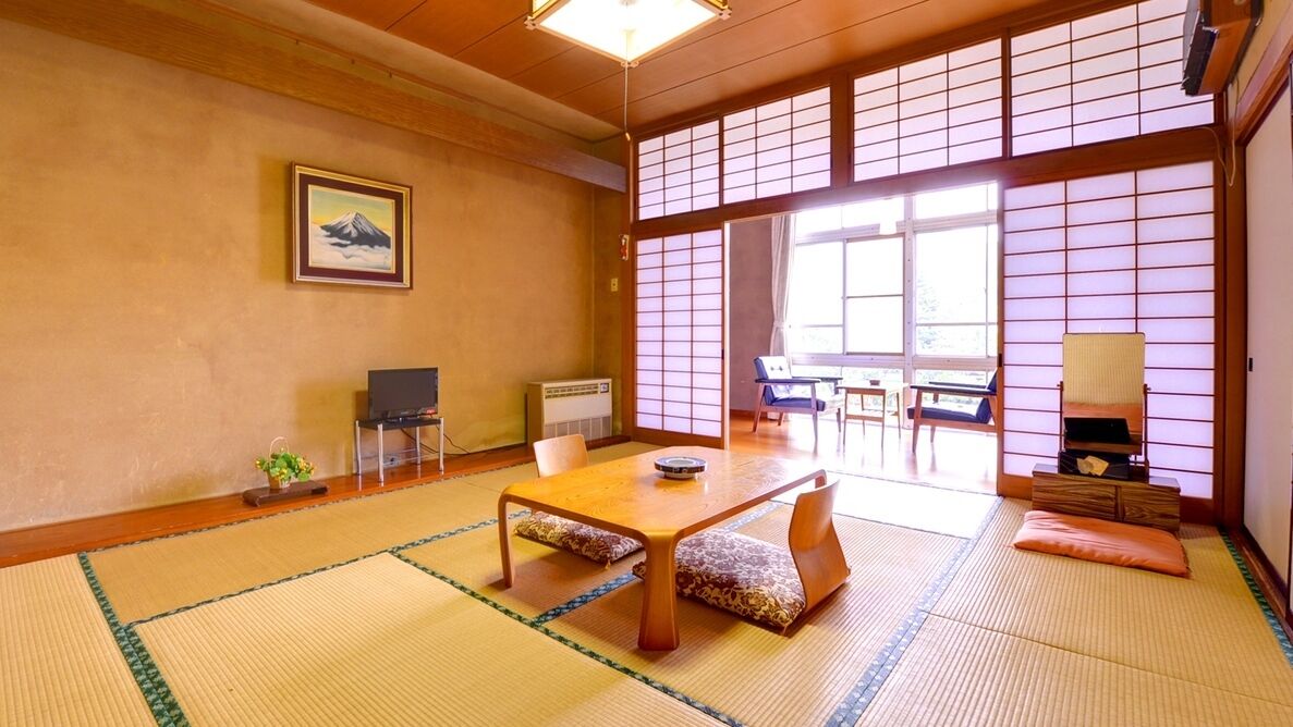 Um quarto japonês tradicional com tatames, uma mesa baixa, cadeiras, uma televisão e portas deslizantes.