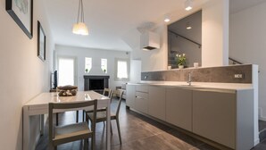 Une cuisine moderne avec un coin repas, comprenant un grand îlot central, un éclairage suspendu et une vue sur le salon.