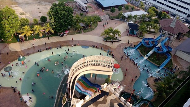 Luchtbeeld van een waterpark met meerdere glijbanen en zwembaden, omringd door gebouwen en groen.