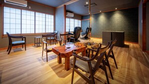 Una habitación con una mesa de comedor de madera, sillas, un sillón de masaje y ventanas amplias.