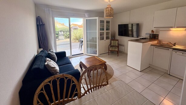 A compact living space with a sofa, dining table, chairs, a kitchen area, and a sliding glass door leading to an outdoor patio.