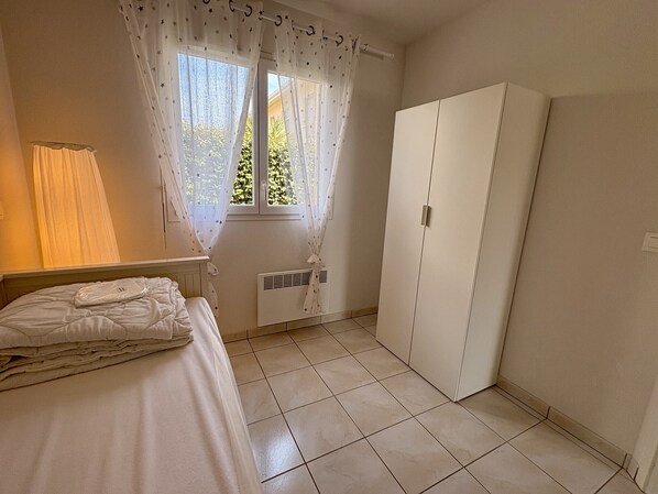 A bedroom with a bed, a wardrobe, a window with star-patterned curtains, and a radiator. - Sympathique maison mitoyenne avec terrasse (125) (Biscarrosse)