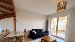A living room with a dining table, chairs, a sofa, a coffee table, and a large window.