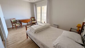 A bedroom with a bed, a wooden chair, a small table, and a window with curtains.