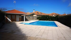 A swimming pool with a tiled deck, a covered area with a roof, and a building with a red-tiled roof.