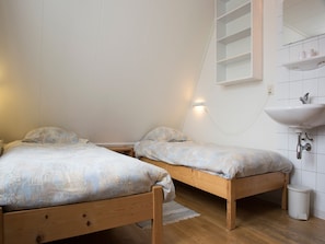 A bedroom with two wooden beds, a white wall-mounted shelf with toiletries, and a white sink.