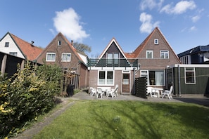 A residential house with a brick facade, a green roof, and a small garden with white chairs and a table.