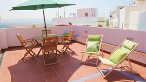 A terrace with a table and chairs, a green umbrella, and a view of the city.