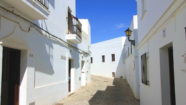 A narrow cobblestone street flanked by white buildings with balconies and windows.