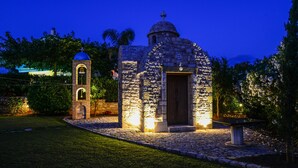Eine steinerne Kapelle mit Glockenturm und Kuppel, umgeben von gepflegten Gärten und einem Pflasterweg.