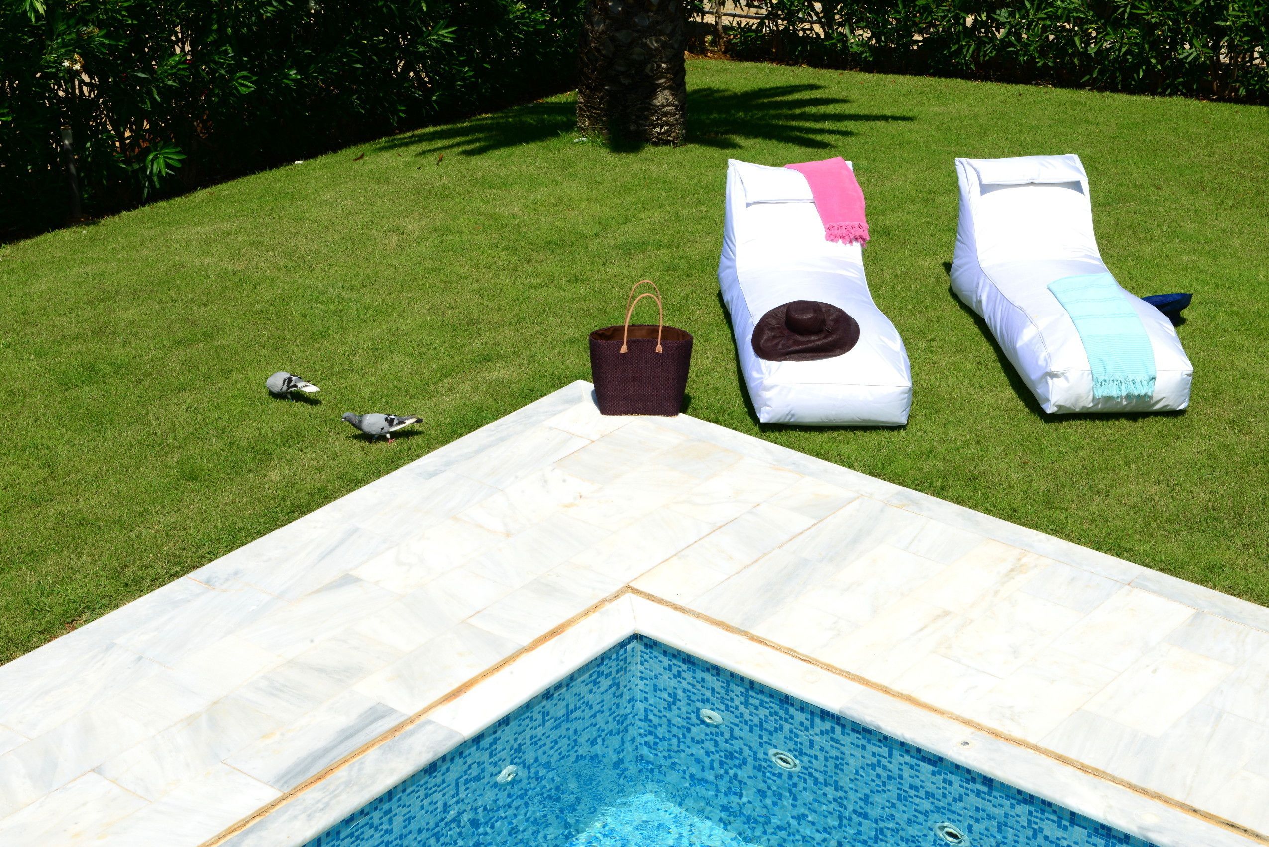 A swimming pool with lounge chairs and a bag on the grass.