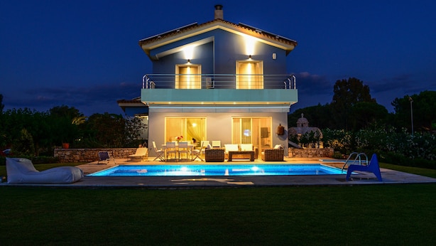 Ein zweistöckiges Haus mit Swimmingpool, Gartenmöbeln und einer Steinmauer.