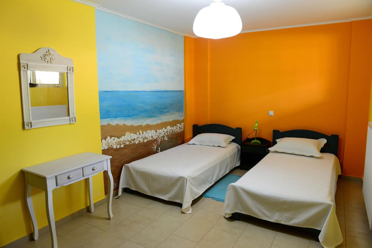 A room with two beds, a small table, and a painting of a beach scene.