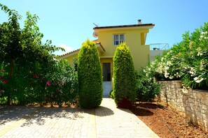 A yellow house with a paved pathway leading to the entrance, surrounded by well-maintained greenery and a stone wall. - Dimitras Villas (Trifylia)