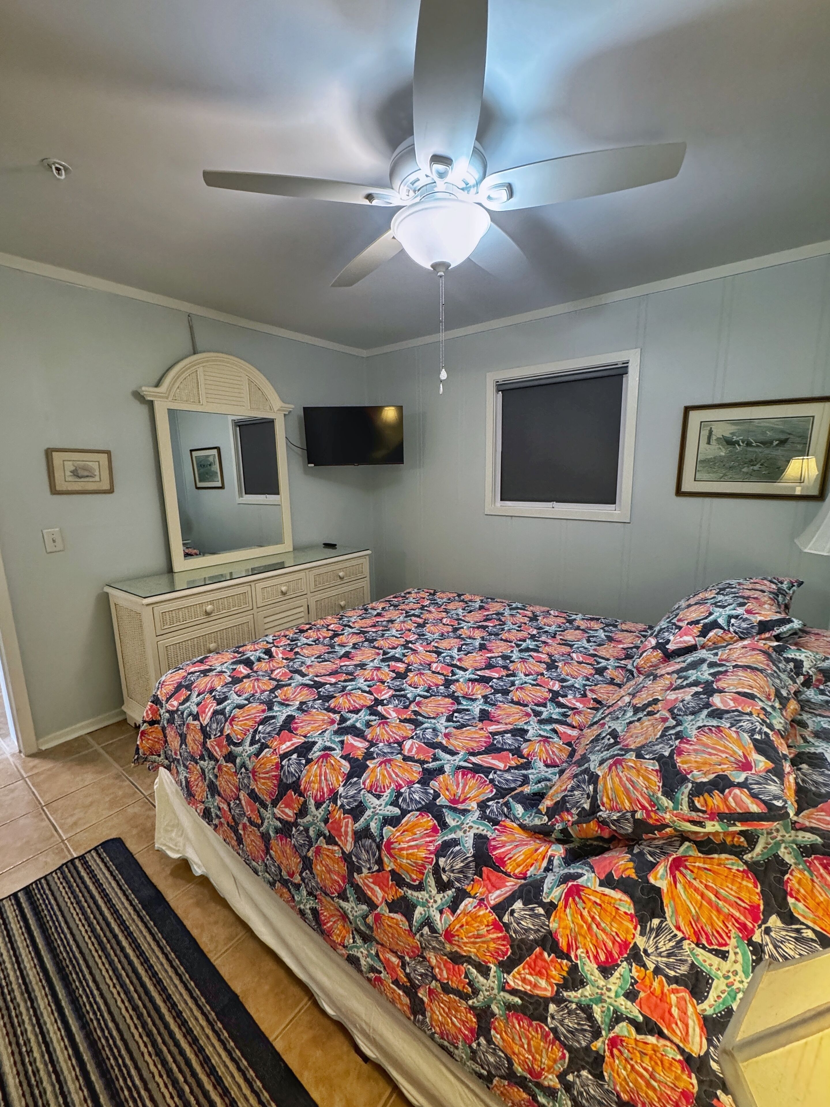 A bedroom with a bed, a ceiling fan, a dresser, a television, and a window.