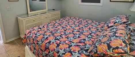 A bedroom with a bed, a ceiling fan, a dresser, a television, and a window.