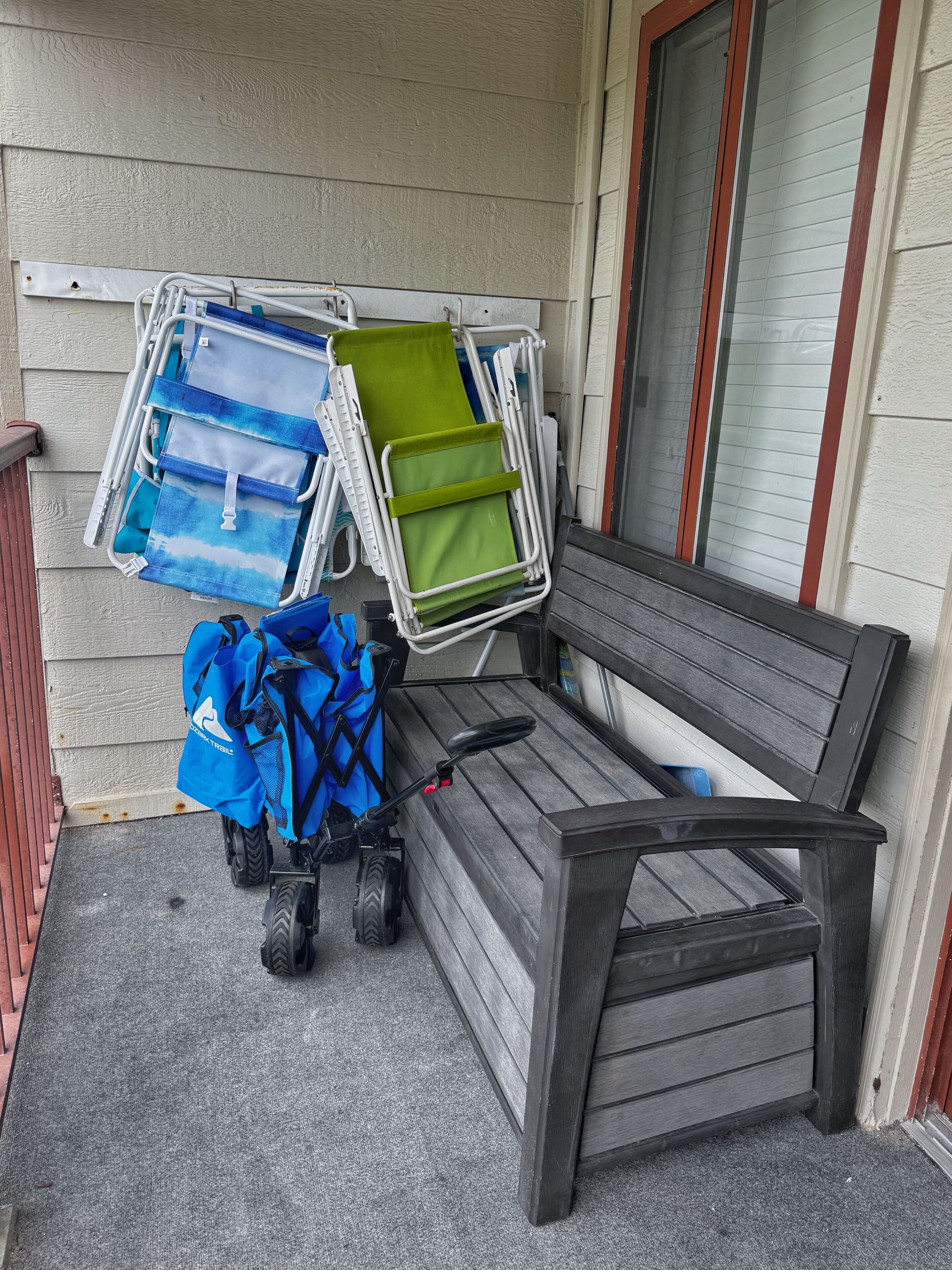 Een bankje met een kinderwagen en opgevouwen stoelen tegen een muur.