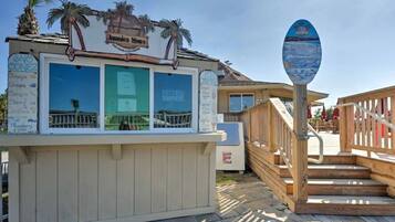 A beachside kiosk with a menu board, a wooden deck, and a signpost.