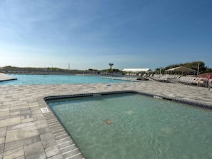 A swimming pool with clear water, a tiled deck, and lounge chairs.