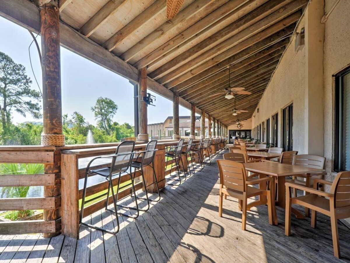 An outdoor covered patio with wooden tables and chairs, a wooden railing, and a view of the surrounding landscape.